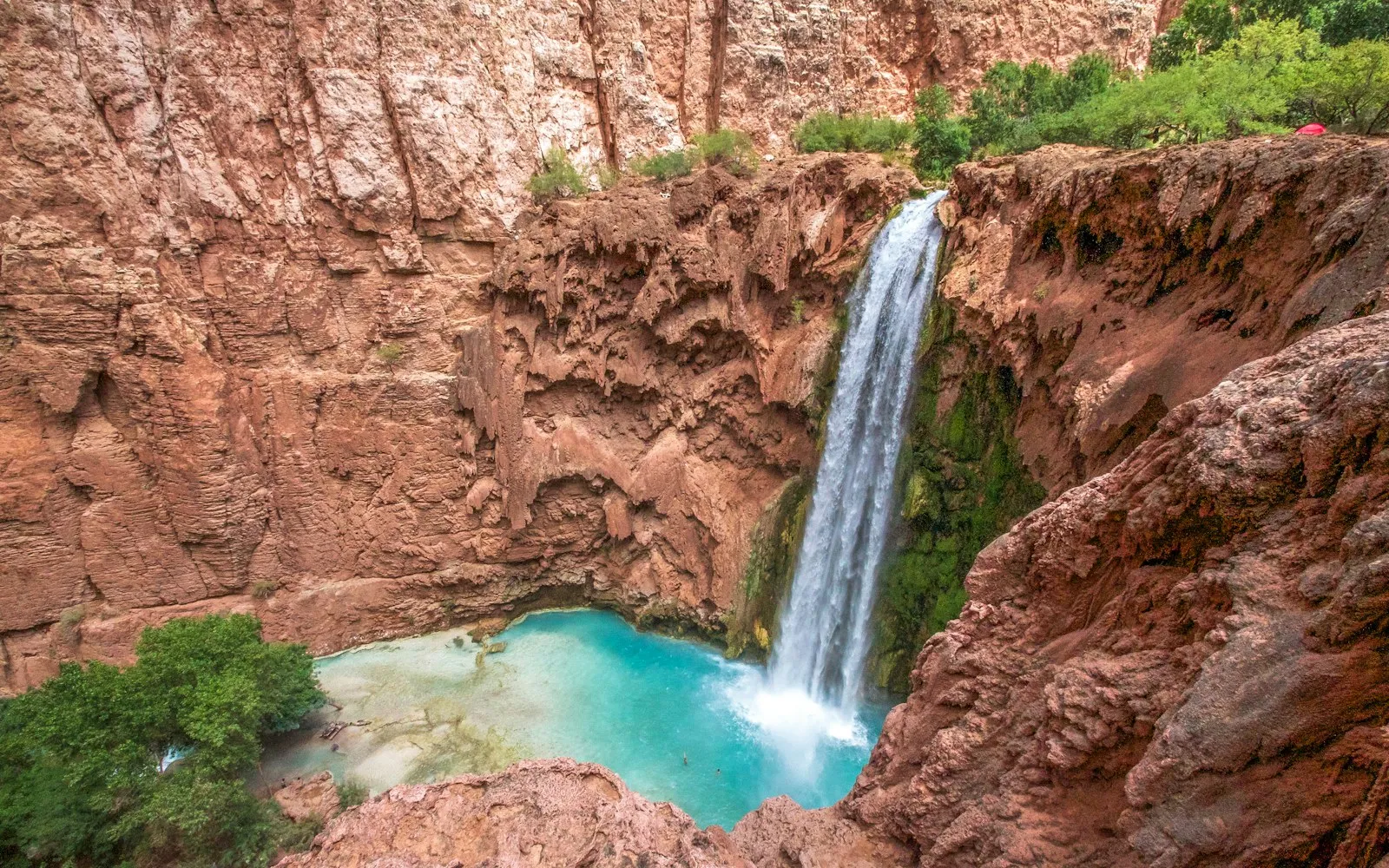 A waterfall pouring into turquoise water between red cliffs