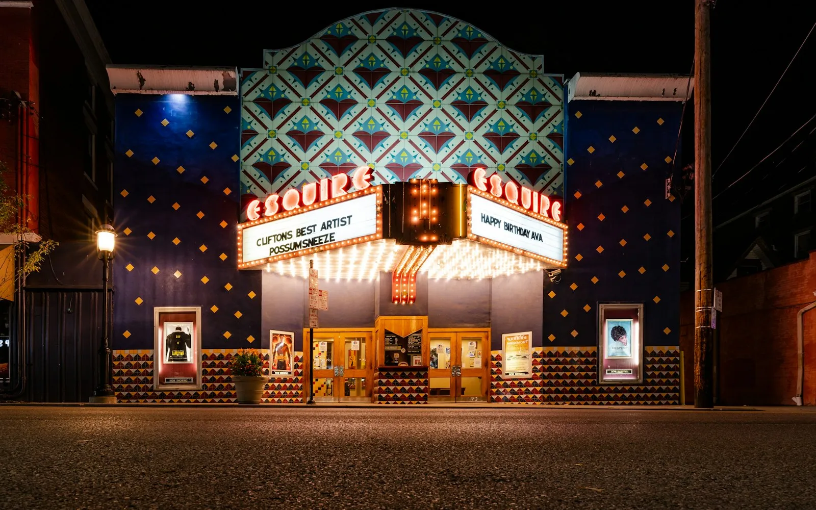 A brightly lit vintage cinema facing an empty street at night