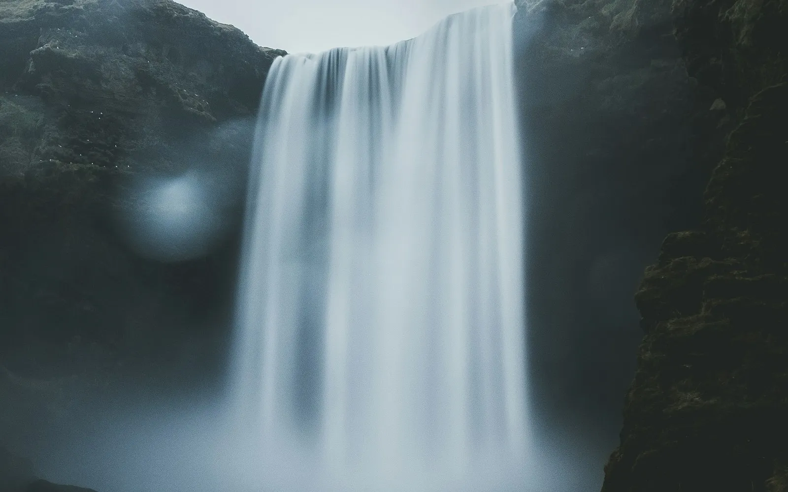 A broad waterfall falling through mist beneath a dark ridge