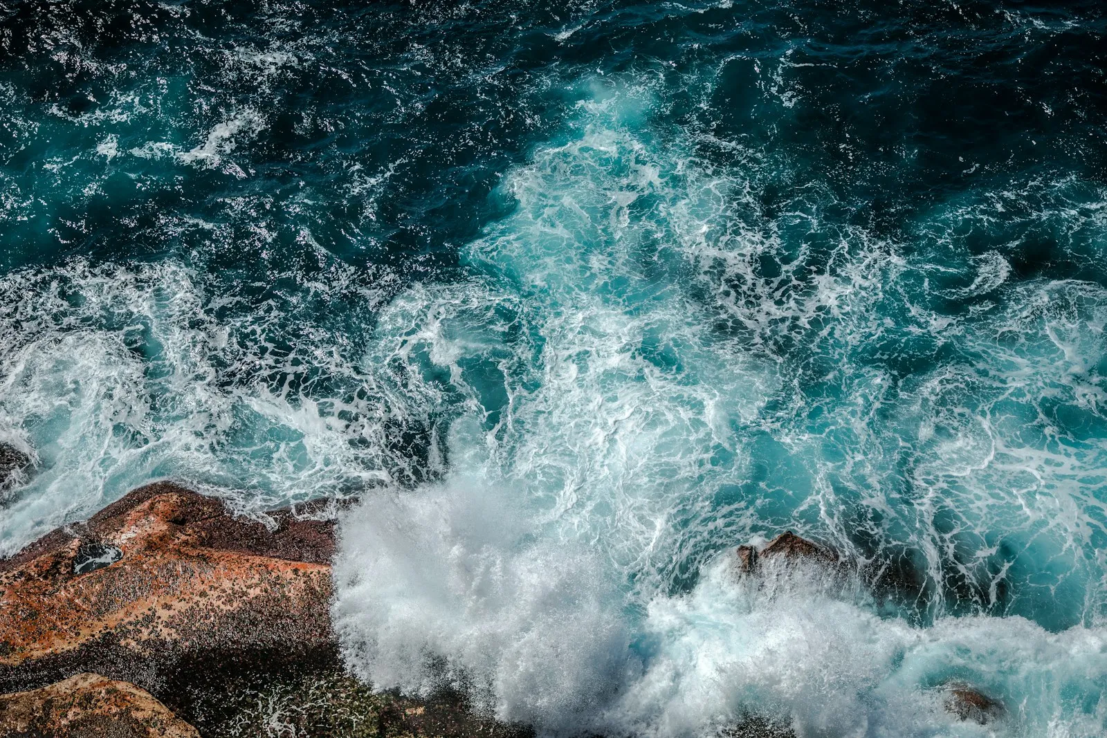 White surf breaking around rocks along a blue coast